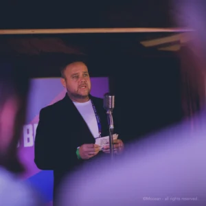 Company culture. A speaker stood in front of an old-fashioned microphone holding presenter cards at a corporate event.